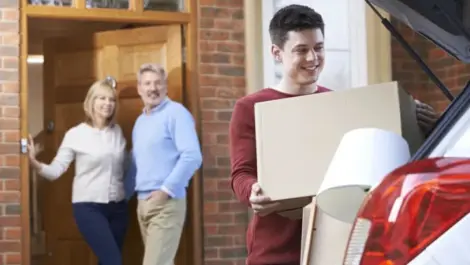 A boy loads a box into an SUV while his parents watch