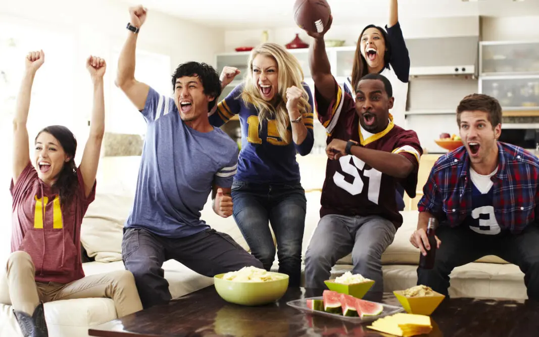 Friends watching football in their living room with snacks