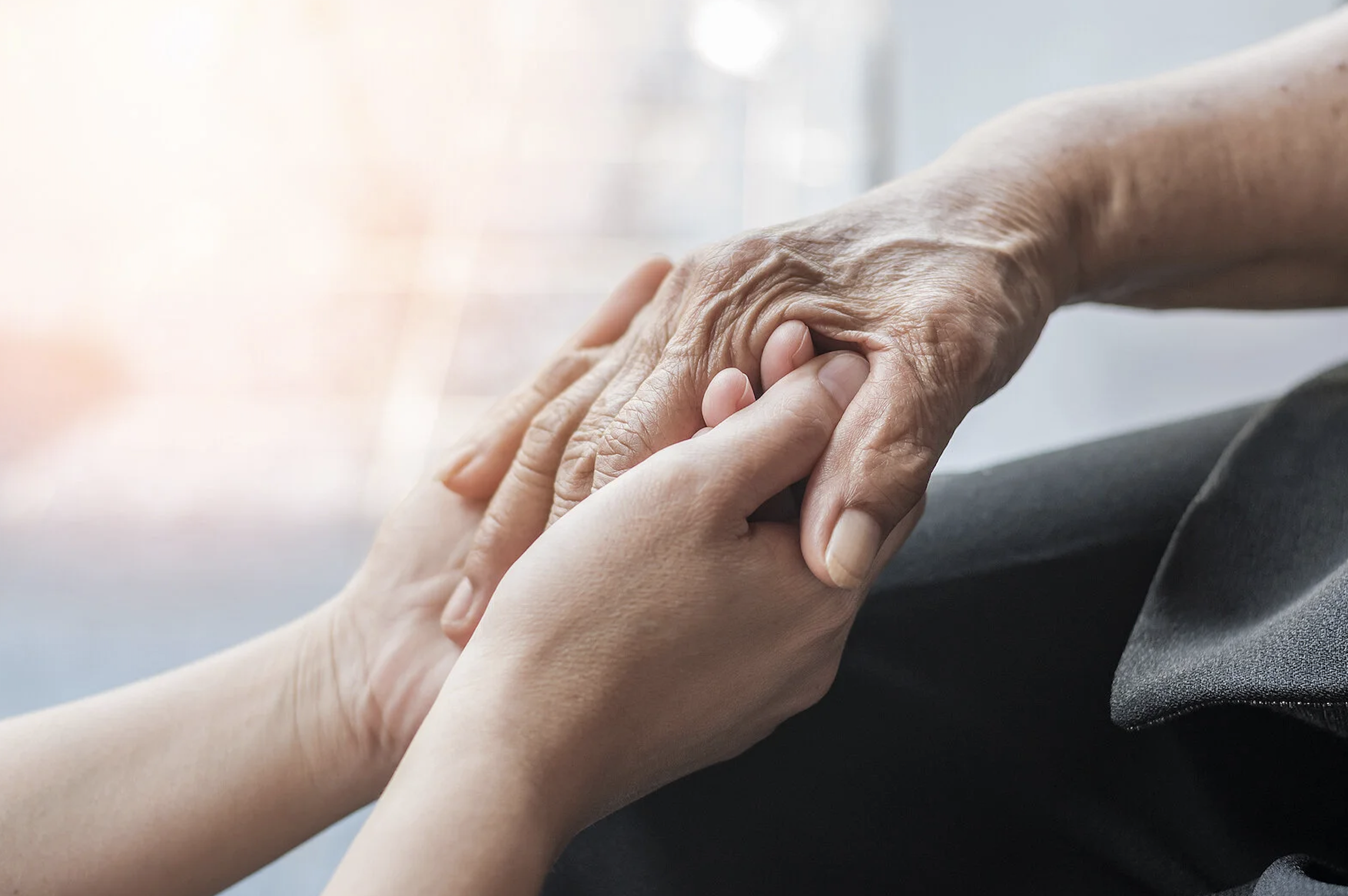 A caregiver holds a loved one's hand for one last goodbye.